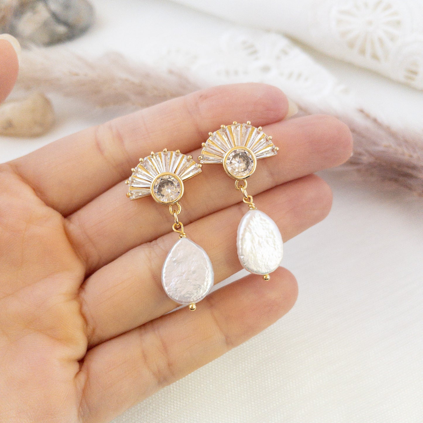 A hand holding a pair of fan shaped posts earrings with freshwater pearls, made by YSM Designs