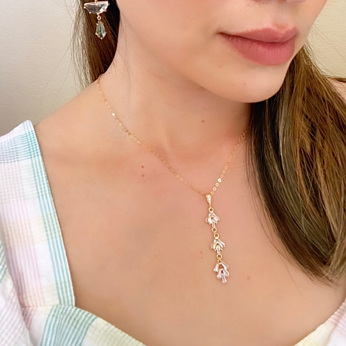 A woman wearing a dainty gold necklace with 3 tiered geometric fan pendant