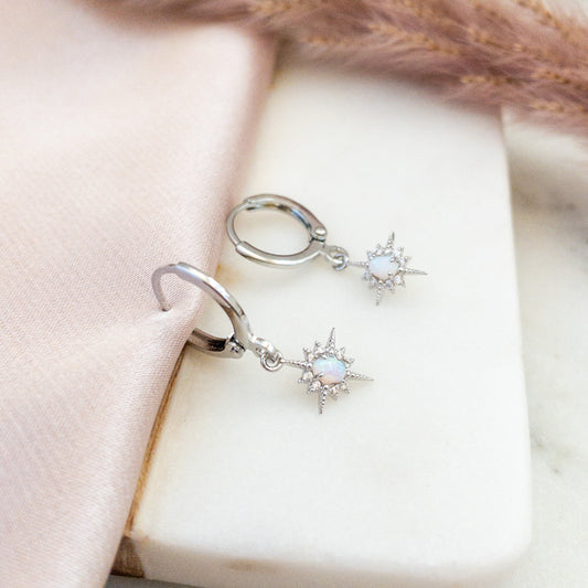 Silver huggie hoop earring with opal north star charms  on a white marble surface