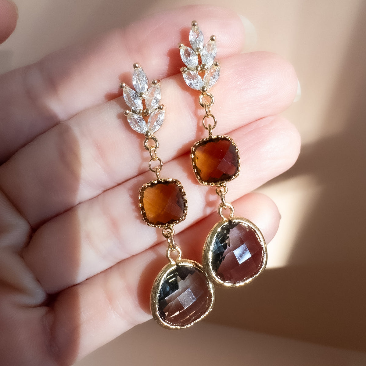 Amber and smoky crystal drop earrings held in hand in warm light