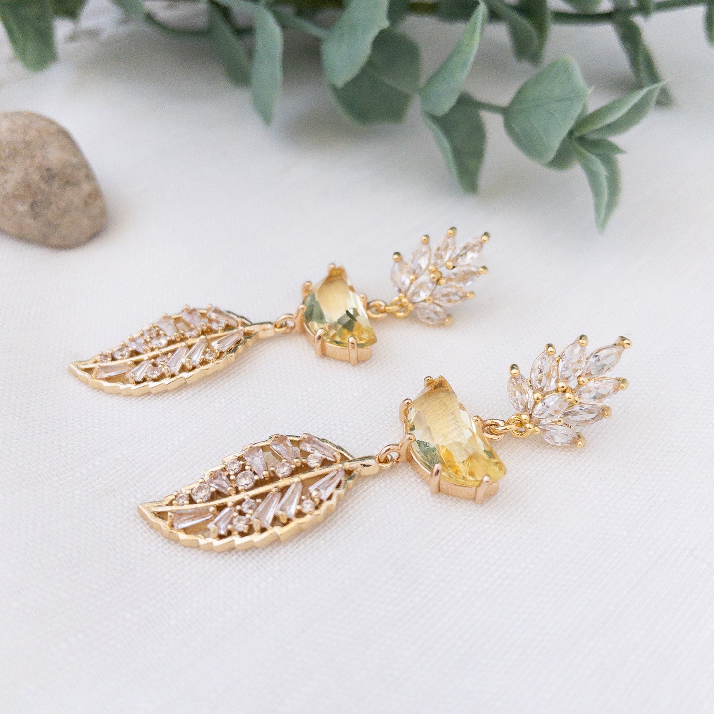 Crystal leaf earrings with yellow stone laying flat on a white surface