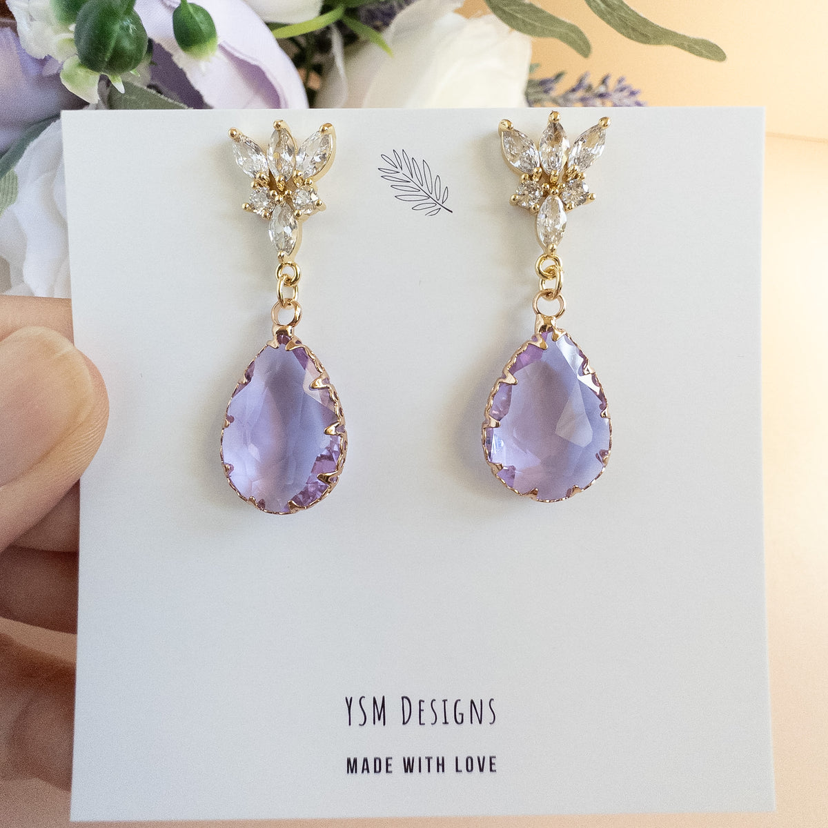 Lavender teardrop earrings on YSM Designs card held in hand to show size