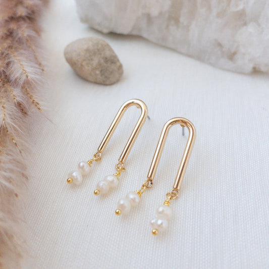 Gold Arch earrings with freshwater pearls laying flat on a white surface