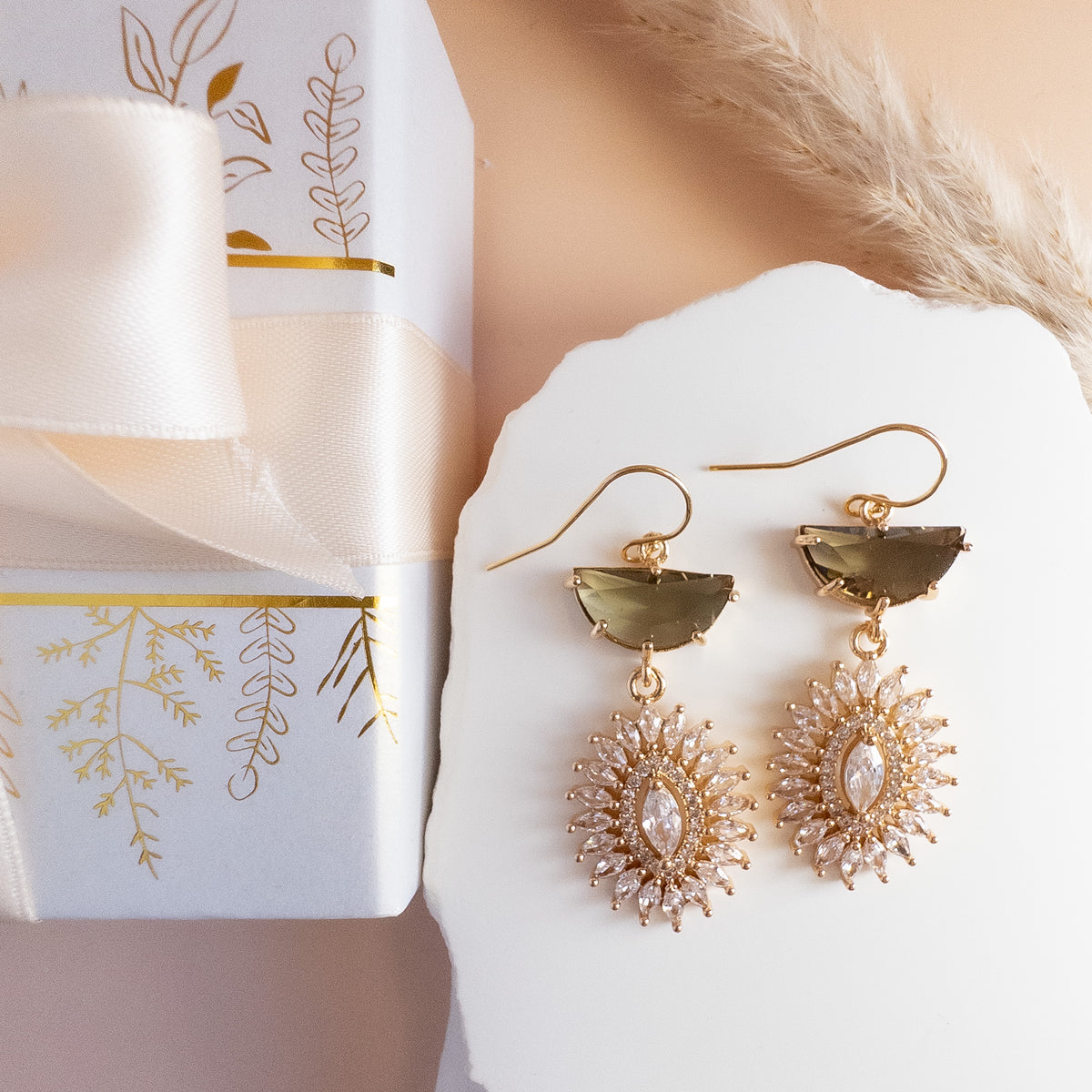 Starburst crystal earrings beside a white gift box with satin ribbon