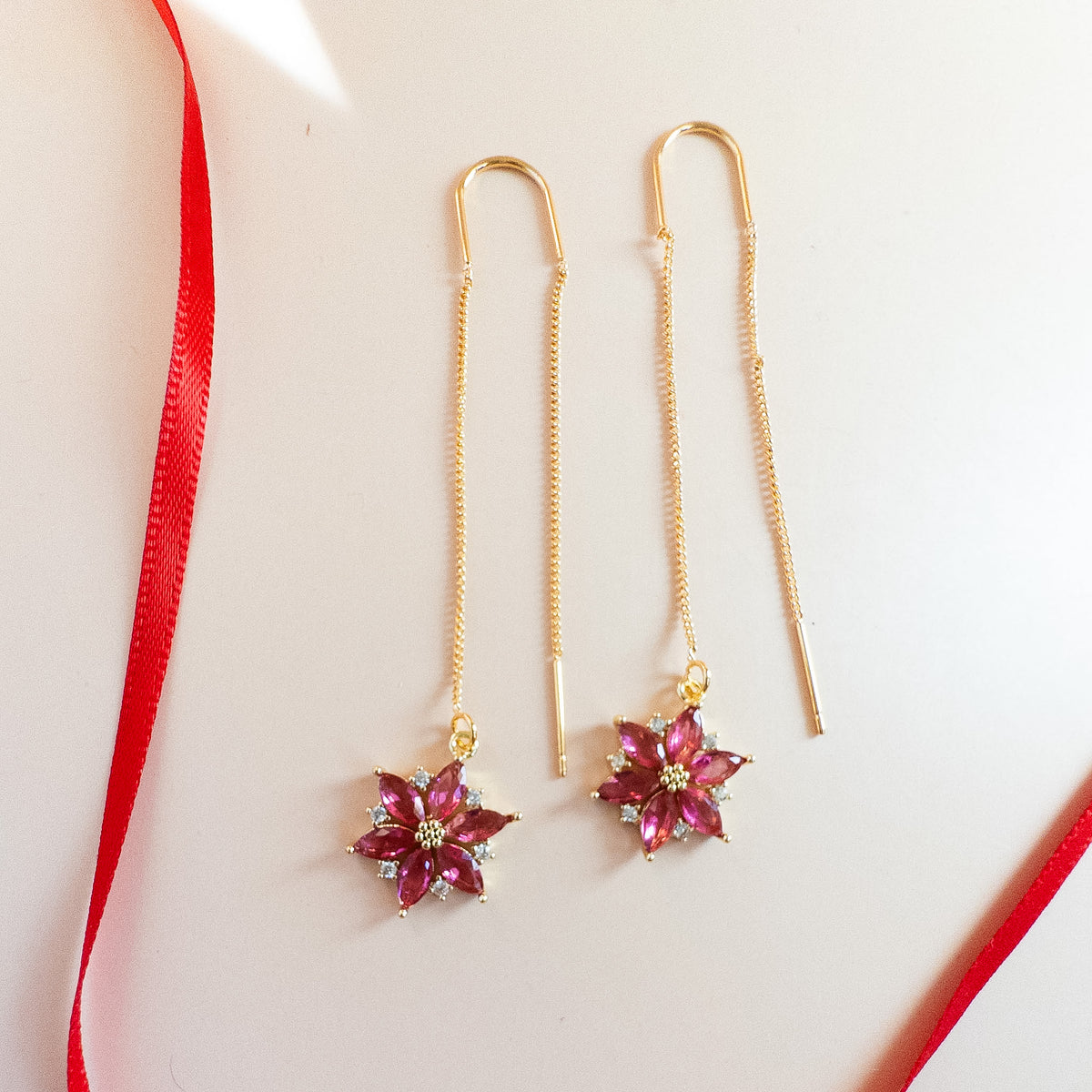 Gold poinsettia threader earrings with cranberry crystals, full length on blush background