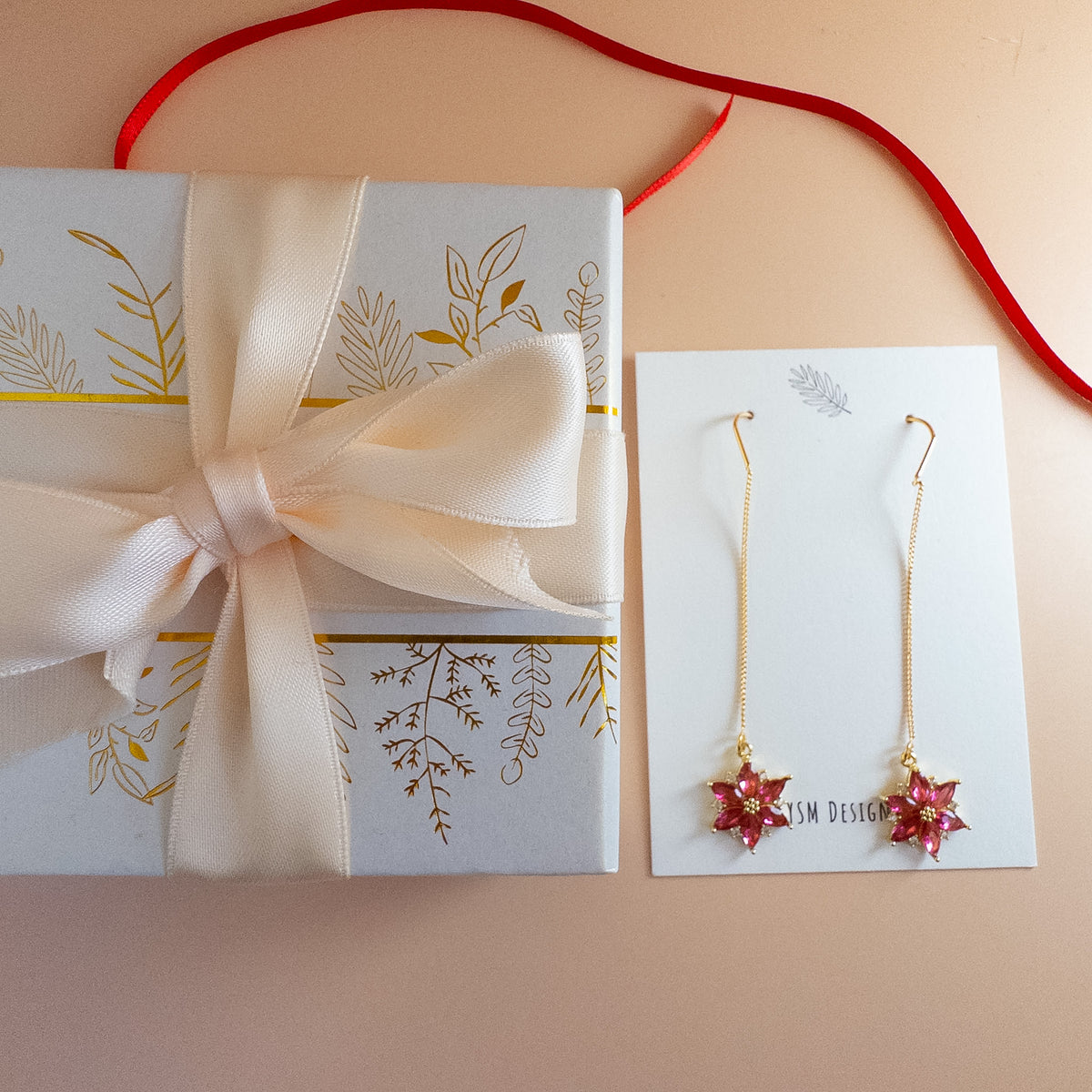 Poinsettia threader earrings on YSM Designs card beside gift box with satin ribbon