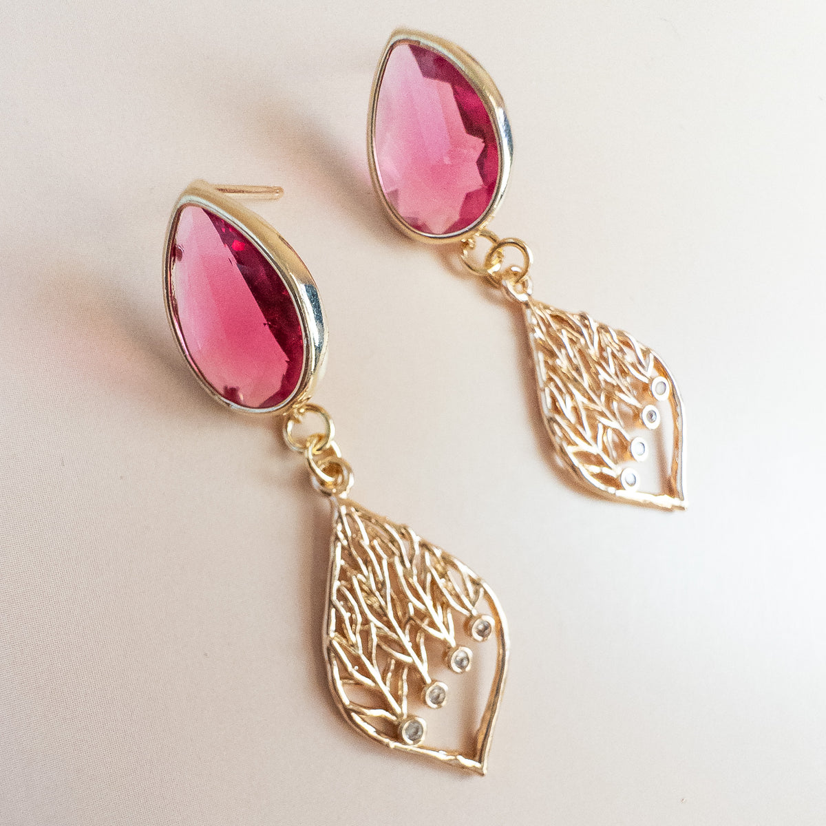 Angled view of raspberry crystal stud earrings with gold leaf dangles
