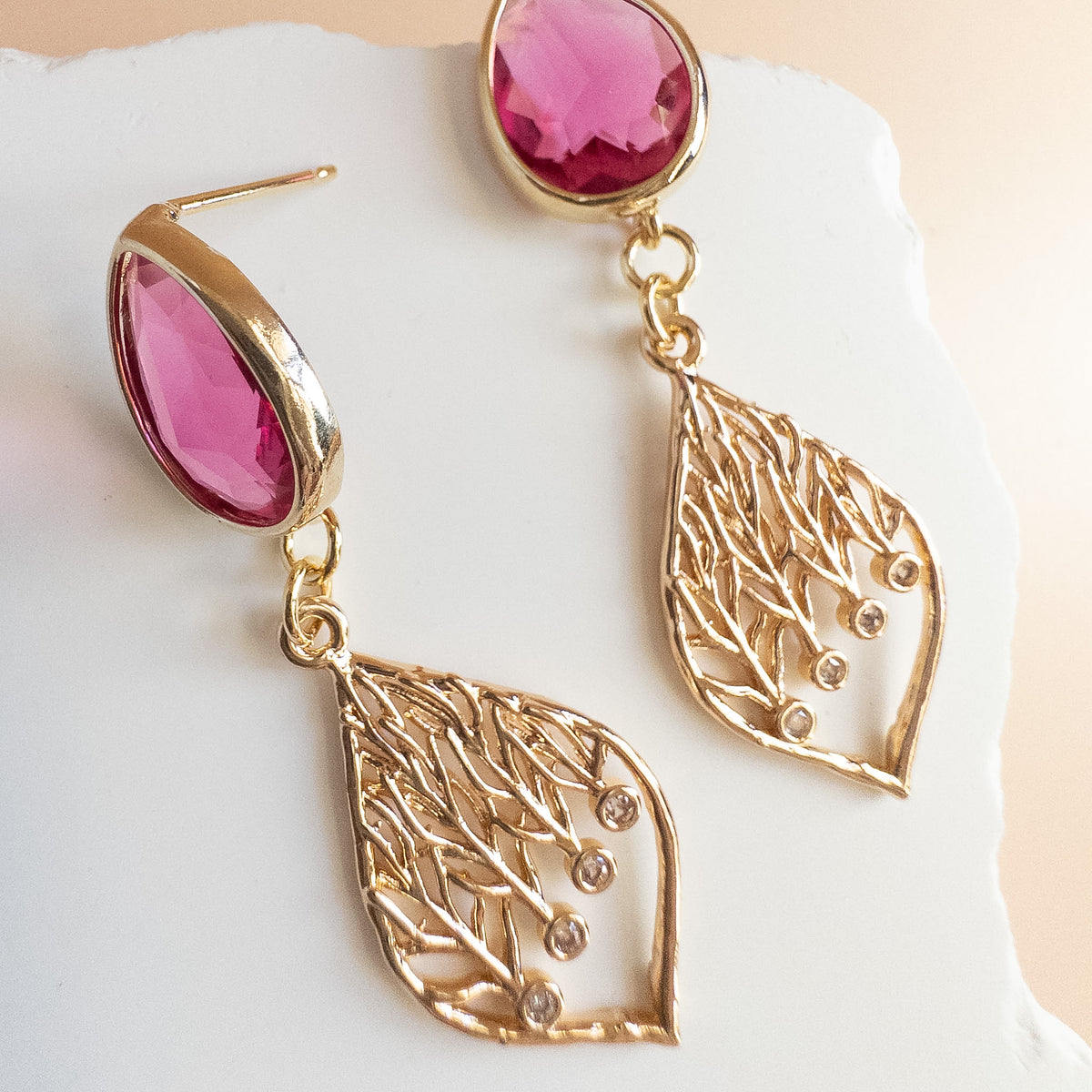 Raspberry crystal teardrop earrings with gold leaf filigree drops on white stone