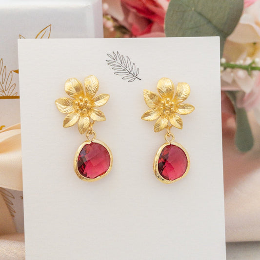 Gold Clematis Flower Post Earrings with red crystal stones on a jewelry card. Earrings by YSM Designs