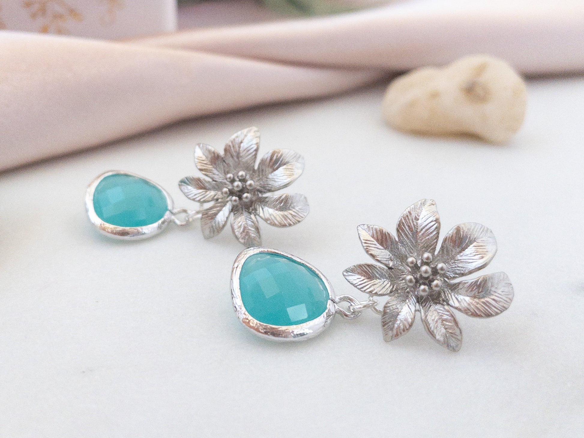 silver Clematis flower earrings with blue stones laying flat on a white surface