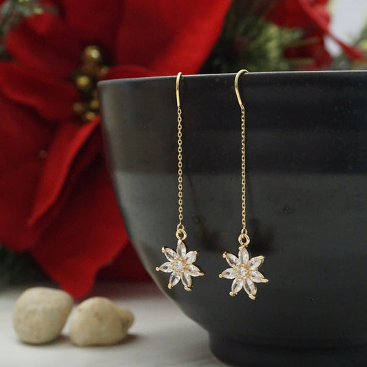 Dainty gold threader earrings with poinsettia charms hanging off a black bowl