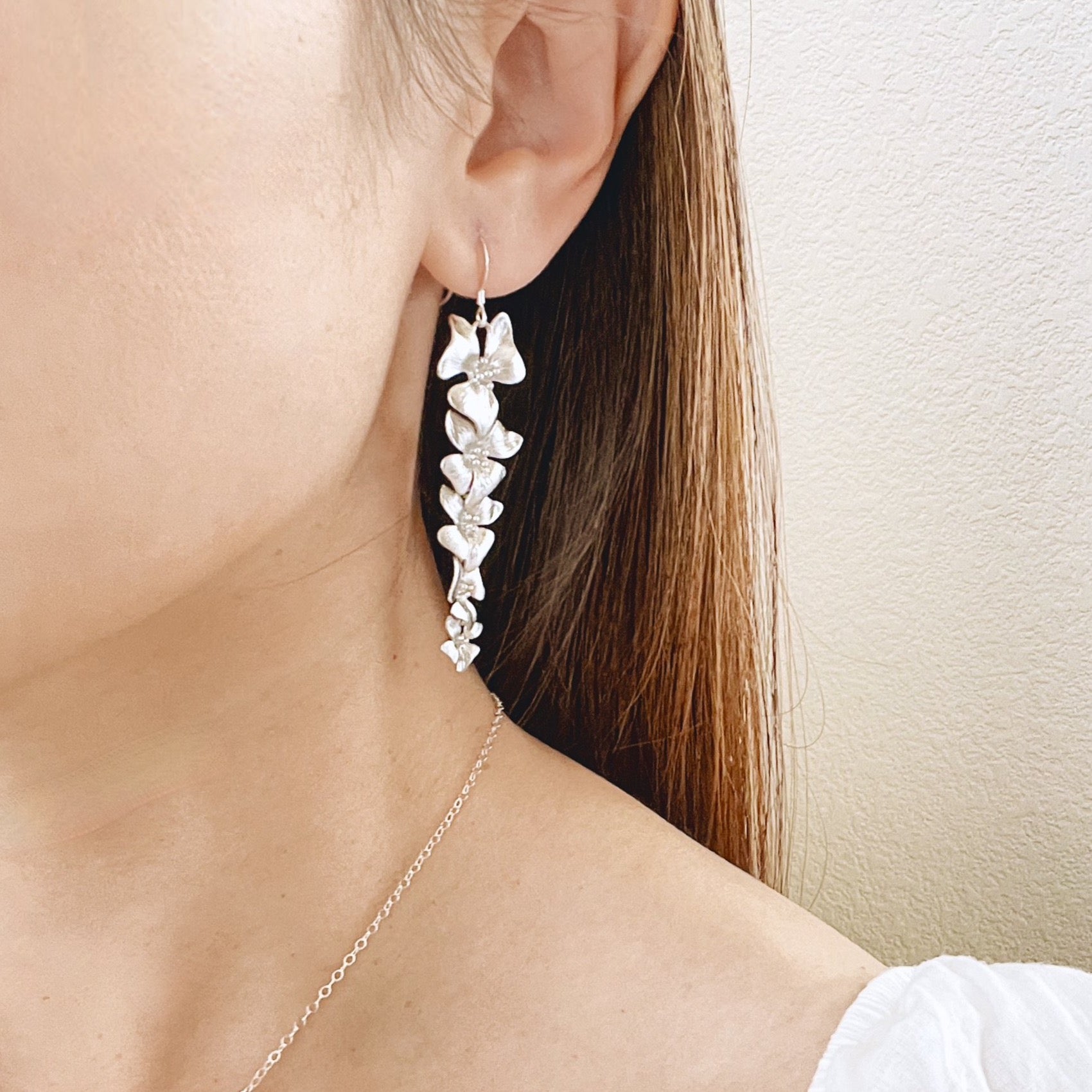 Woman wearing long silver dogwood flower earrings