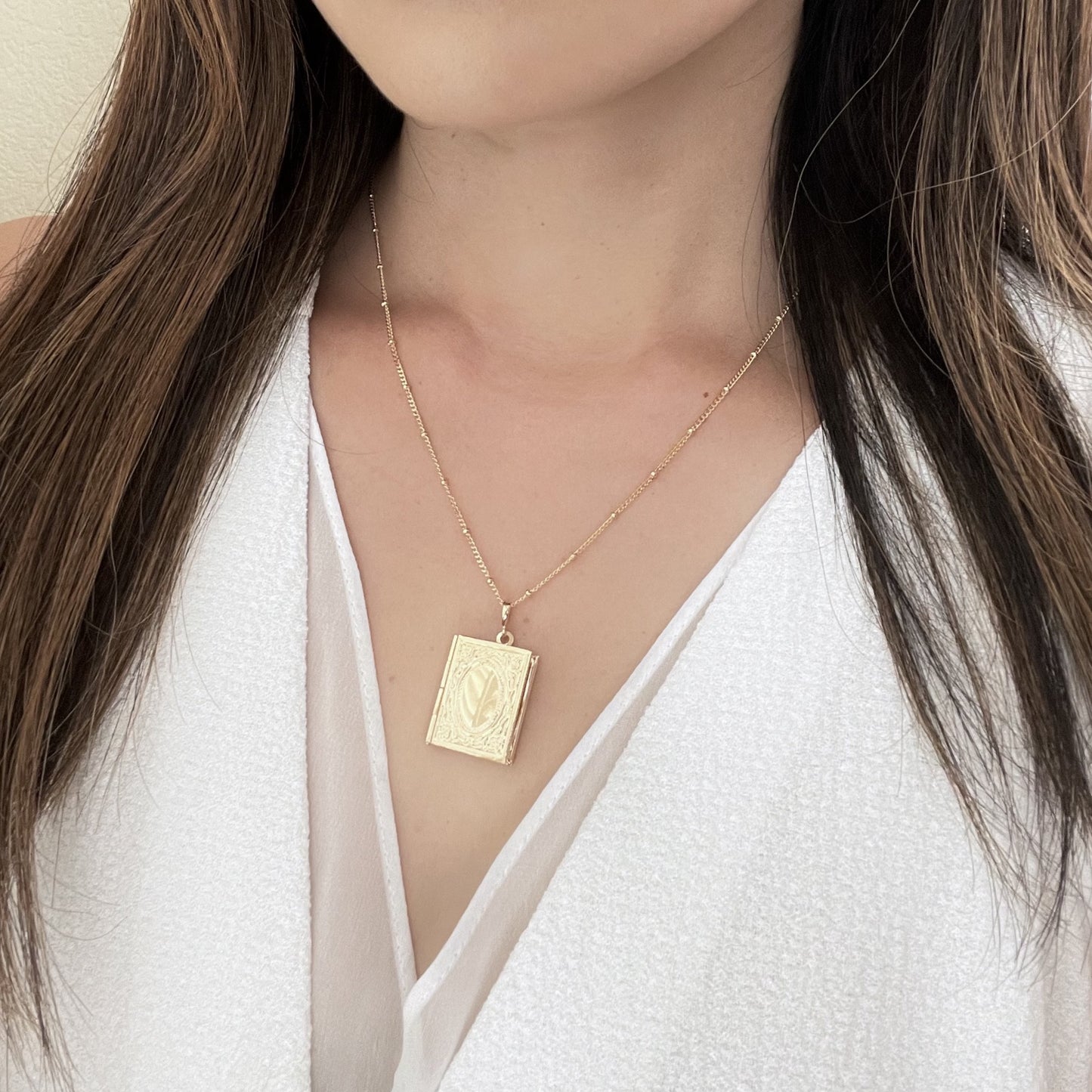 Woman wearing gold rectangular locket necklace