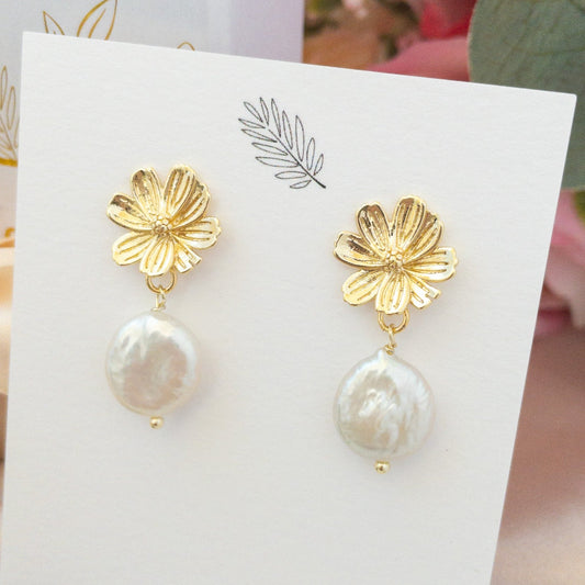 Gold Sakura flower post earrings with white freshwater pearls on a jewelry card. Earrings by YSM Designs